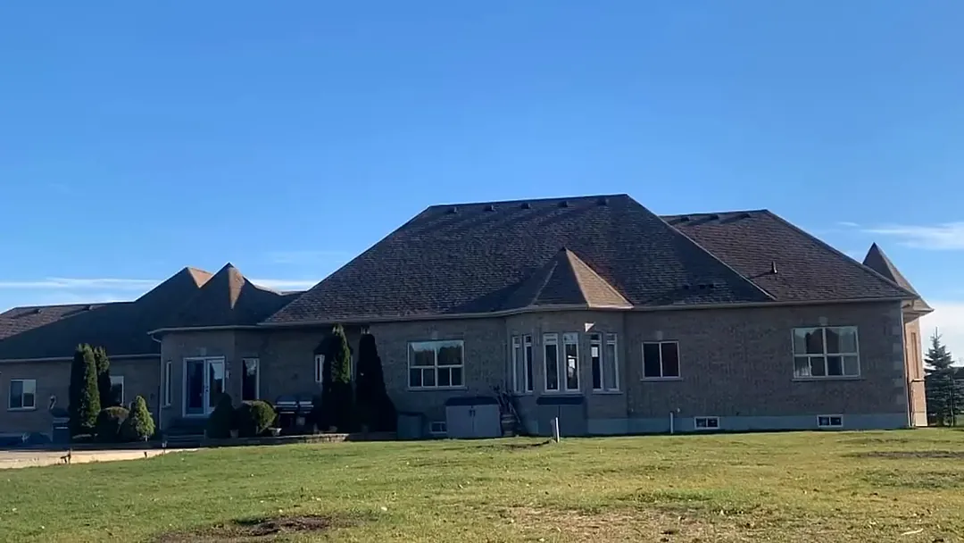 A brick home with a finished dark asphalt shingle roof under a clear sky