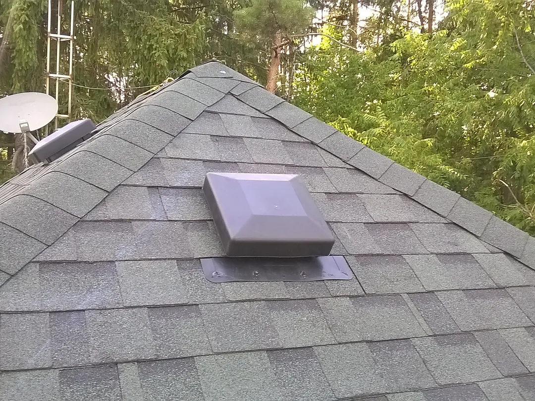 Close view of a roof peak with ridge cap shingles and a roof vent