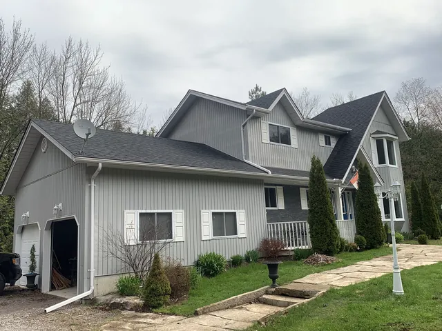 Grey board-and-batten two-storey home with a new dark shingle roof