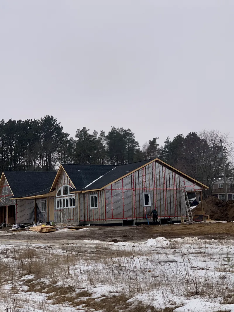 A new home under construction in winter with its roof shingled and walls wrapped